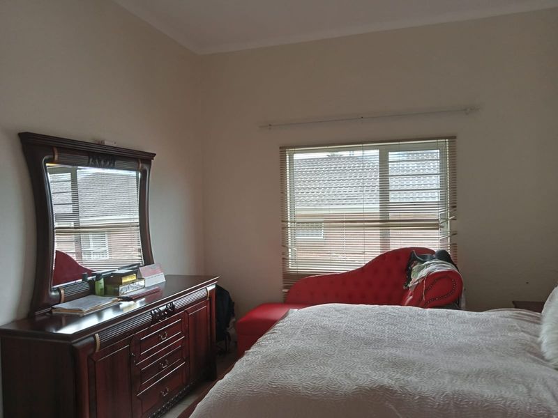 A bedroom featuring neutral walls, a window with fitted venetian blinds, and a curtain rod, providing a functional and well-lit living space.