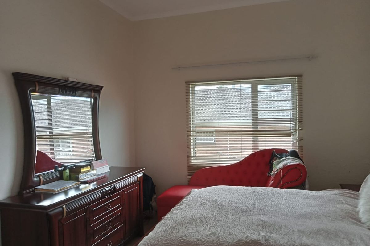 A bedroom featuring neutral walls, a window with fitted venetian blinds, and a curtain rod, providing a functional and well-lit living space.