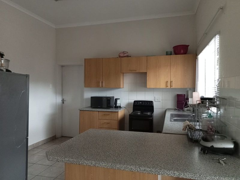 A functional kitchen featuring laminate cabinetry, granite-look countertops, tiled splashbacks, and a freestanding electric stove with a breakfast bar area.