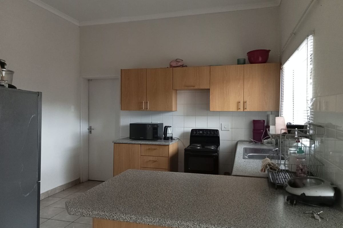 A functional kitchen featuring laminate cabinetry, granite-look countertops, tiled splashbacks, and a freestanding electric stove with a breakfast bar area.