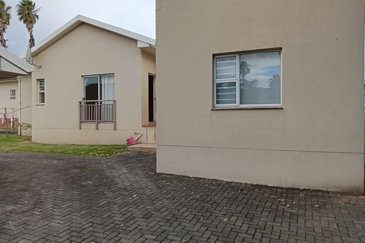 Rear view of the townhouse featuring paved driveway, neutral exterior walls, and aluminium window frames.