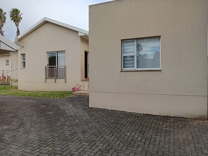 Rear view of the townhouse featuring paved driveway, neutral exterior walls, and aluminium window frames.