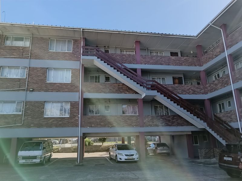 Exterior view of a multi-story apartment complex featuring brick facade, external staircases, and ground-level covered parking bays.