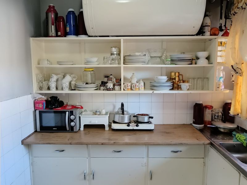 A compact kitchen area featuring built-in cabinetry, open shelving, a tiled backsplash, and a stainless steel sink with a laminate countertop.