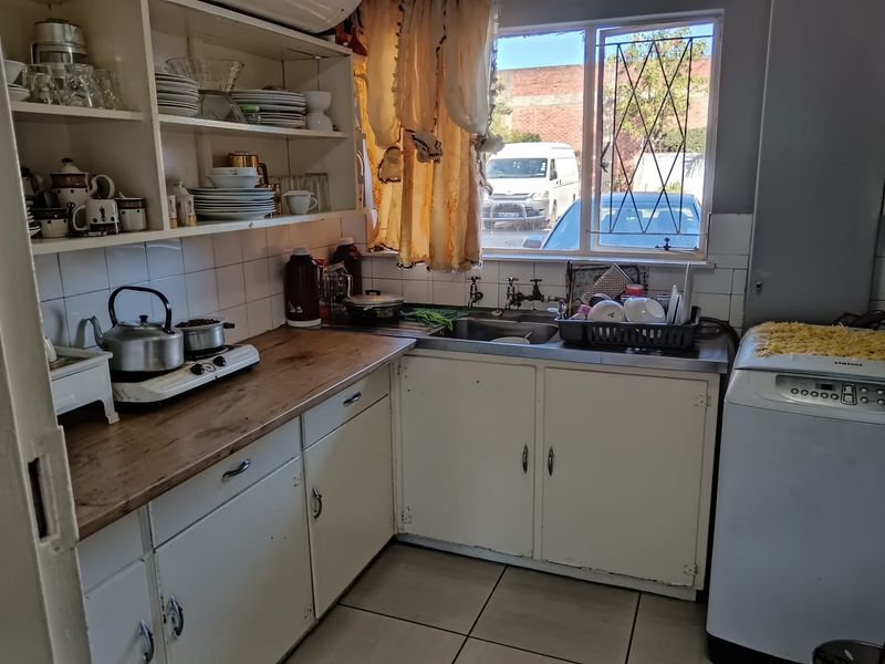 A functional kitchen featuring built-in cabinetry, a stainless steel sink, tiled backsplash, and ceramic flooring, offering potential for modernization and aesthetic updates.