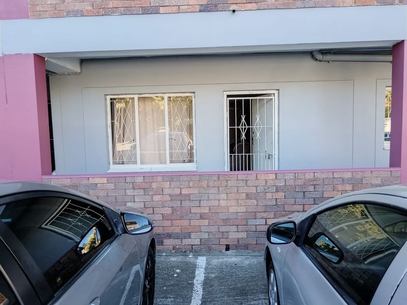 Exterior view of an apartment unit featuring a brick facade, security gate, and security bars on the windows, with dedicated parking space.
