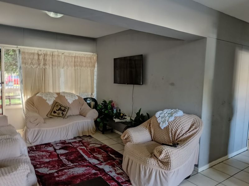 A living room area featuring tiled flooring and a wall-mounted television setup, requiring minor cosmetic updates to the wall finishes.