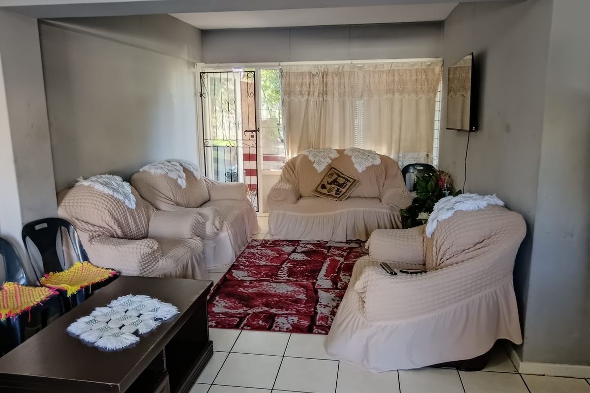 A living room featuring tiled flooring and a security gate leading to an outdoor area, providing a functional space with potential for cosmetic updates.