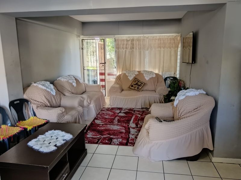 A living room featuring tiled flooring and a security gate leading to an outdoor area, providing a functional space with potential for cosmetic updates.