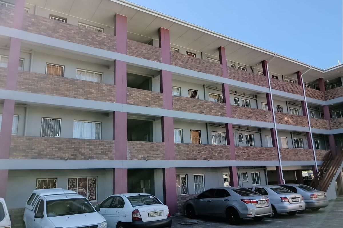 Exterior view of a multi-story apartment building featuring brick facade detailing, security bars on windows, and open-air walkways.