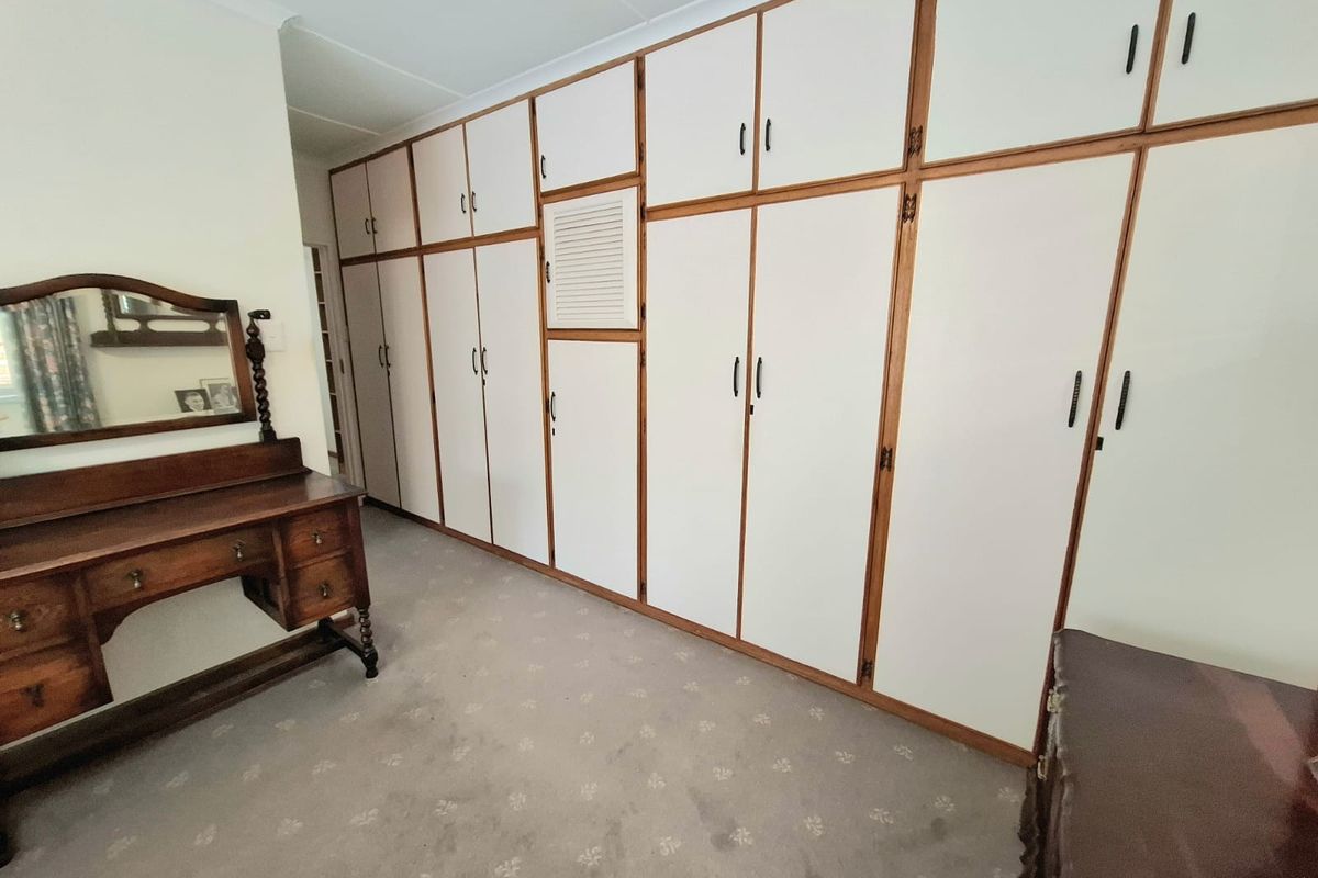 A bedroom featuring extensive floor-to-ceiling built-in cupboards with timber trim and neutral carpeting.