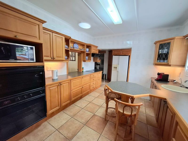 A spacious kitchen featuring traditional timber cabinetry, laminate countertops, built-in oven, and tiled flooring, offering a functional layout with ample storage space.