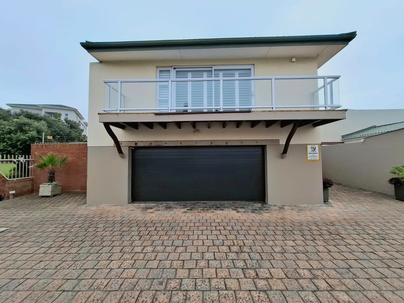 Front exterior view featuring a paved driveway, a single garage door, and an elevated balcony with a glass balustrade.