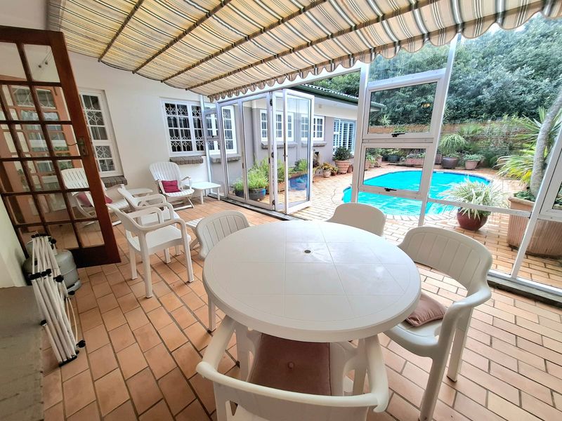 Covered patio area featuring tiled flooring, a retractable awning, and direct access to a swimming pool and garden through folding glass doors.
