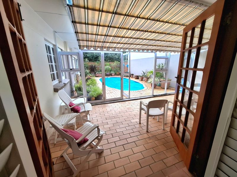 Covered patio area featuring tiled flooring and a retractable awning, providing seamless access to the outdoor swimming pool and garden space.