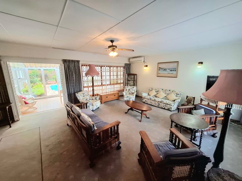Spacious living room featuring a ceiling fan, split system air conditioning, and large sliding glass doors providing direct access to the outdoor patio and pool area.