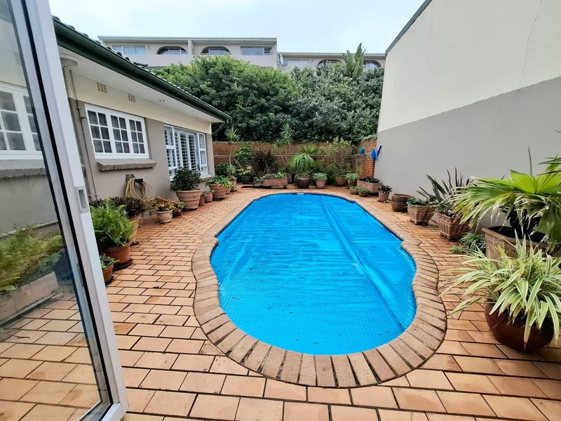 A private outdoor pool area featuring brick paving, a swimming pool with a cover, and perimeter boundary walls.