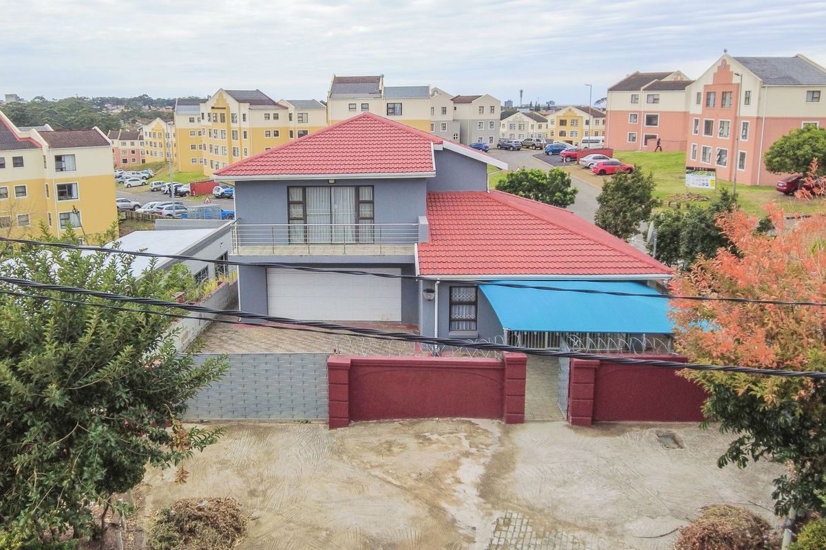 Aerial view of a two-story residential house featuring a tiled roof, balcony, garage, and a secure perimeter wall with gated access.
