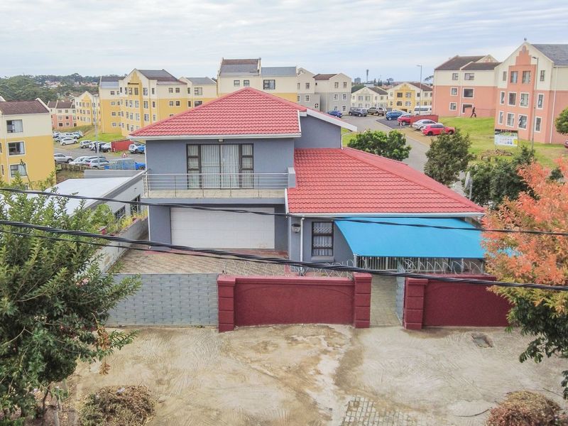 Aerial view of a two-story residential house featuring a tiled roof, balcony, garage, and a secure perimeter wall with gated access.