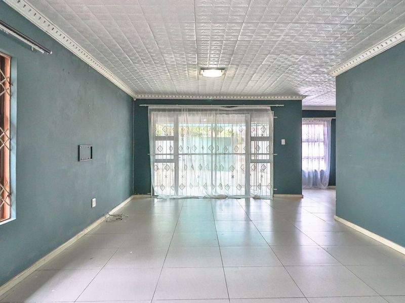 Spacious, empty living area featuring tiled floors, a textured ceiling with cornice detailing, and large sliding doors providing access to the exterior.