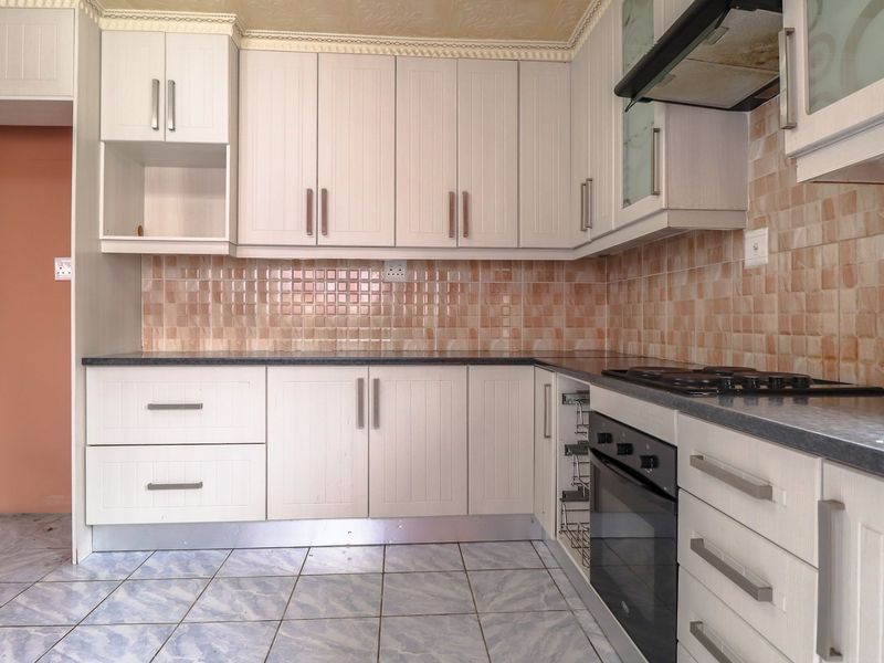A functional kitchen featuring white built-in cabinetry, laminate countertops, a tiled backsplash, and integrated cooking appliances including an oven and gas hob.