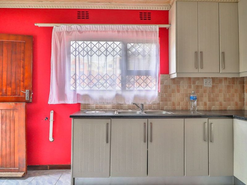 A functional kitchen area featuring built-in cabinetry, a stainless steel sink, tiled backsplash, and a stable door, offering a blank canvas for renovation.