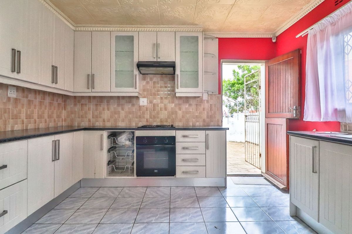 A functional kitchen featuring white built-in cabinetry, tiled backsplash, integrated oven and hob, and direct access to the exterior via a timber door.