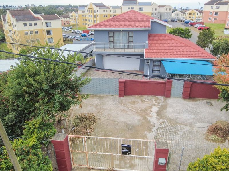 Aerial view of a two-story residential property featuring a tiled roof, paved driveway, secure boundary wall, and an upper-level balcony.
