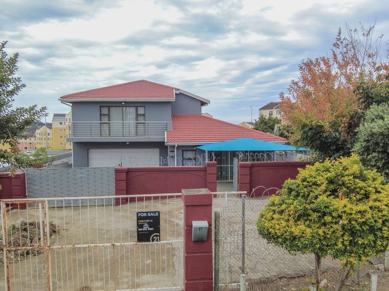 Front view of a two-story house featuring a red tiled roof, a balcony, a garage, and a secure perimeter wall with a gated entrance.