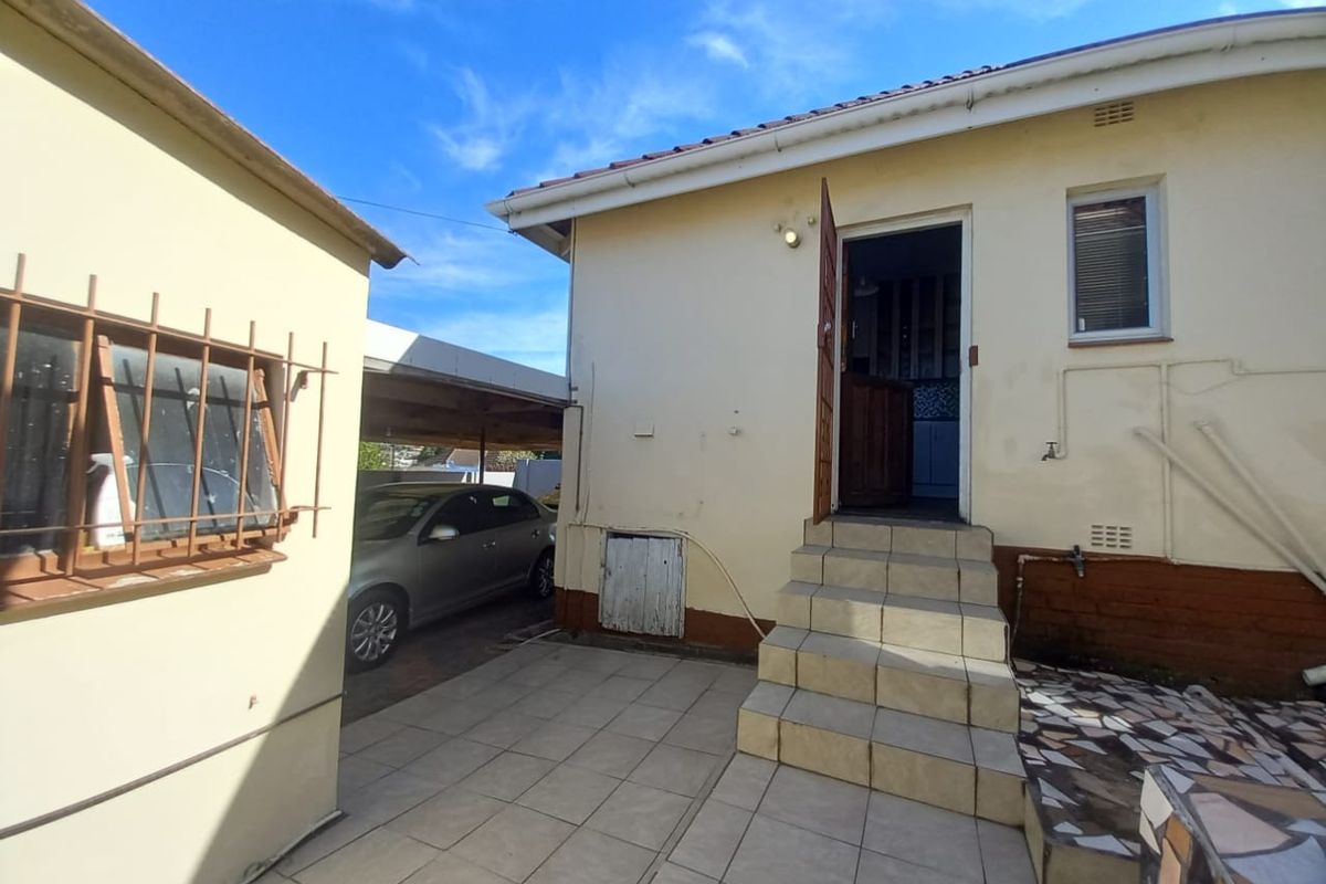 Rear exterior view showing a tiled patio area, concrete steps leading to the entrance, and an adjacent carport structure.