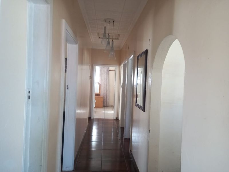 A long hallway featuring tiled flooring, an arched entryway, and ceiling tiles, providing access to multiple rooms within the home.
