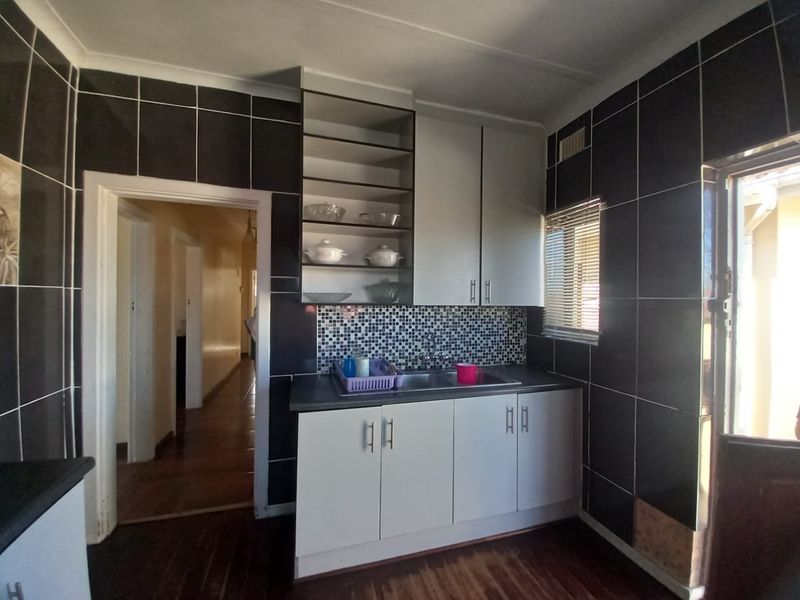 A compact scullery or prep area featuring built-in cabinetry, a stainless steel sink, and dark tiled walls, providing functional utility space.