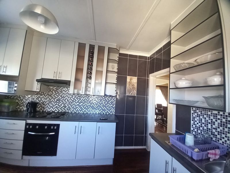 Functional kitchen featuring built-in cabinetry, mosaic tile backsplash, integrated oven, electric hob, and ample storage space with a connected dining area.