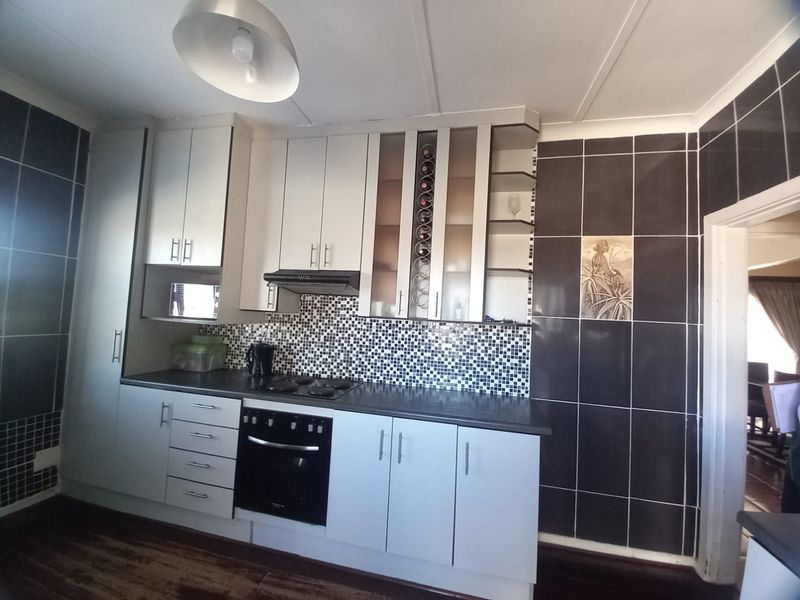 A functional kitchen featuring built-in cabinetry, a mosaic tile backsplash, integrated oven, hob, and extractor fan with a wine rack display.