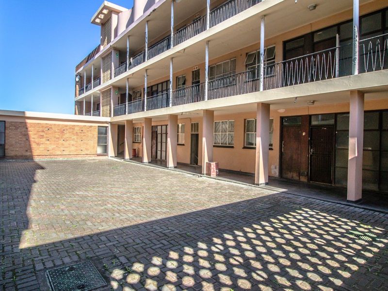 A multi-story apartment building exterior featuring a paved courtyard and shared balcony access with metal railings.