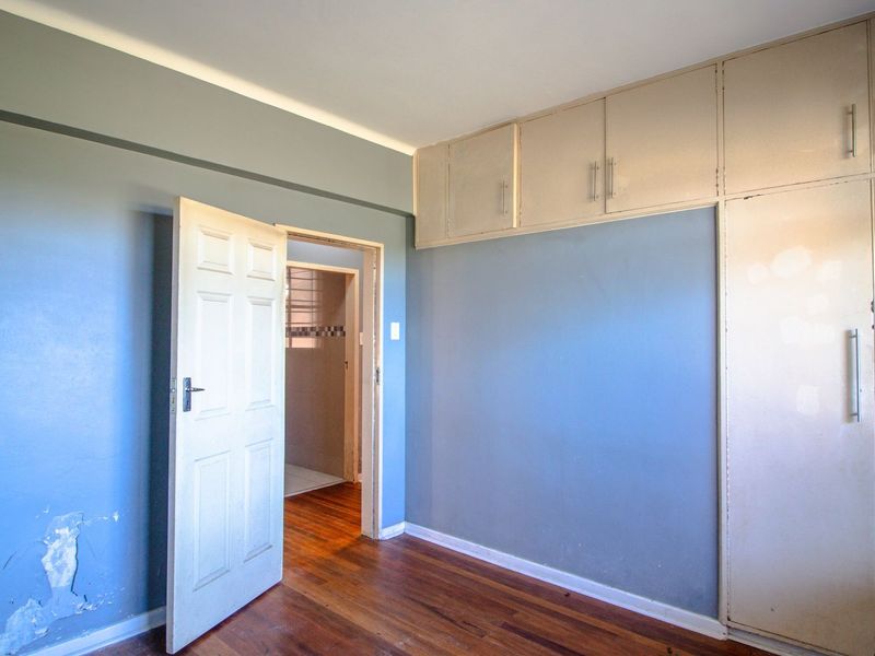 An empty bedroom featuring hardwood flooring, built-in cupboards, and blue painted walls with visible surface wear.