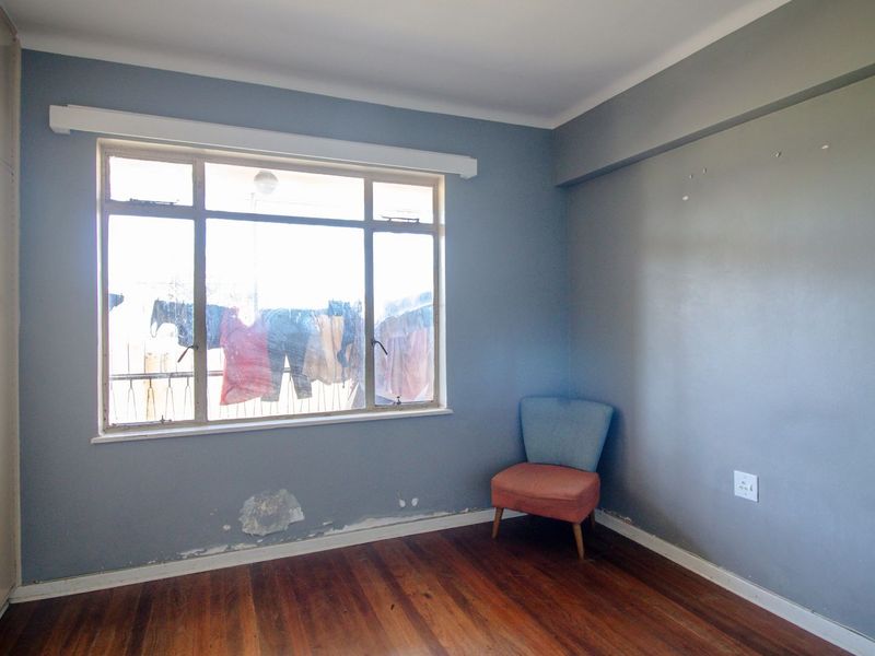 A bedroom featuring timber flooring, built-in cupboards, and a large window. The room requires minor wall repairs and cosmetic updates.