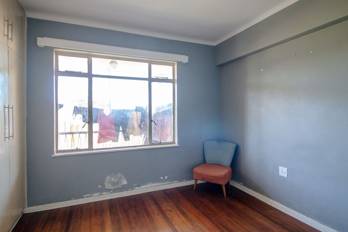 A bedroom featuring timber flooring, built-in cupboards, and a large window. The room requires minor wall repairs and cosmetic updates.