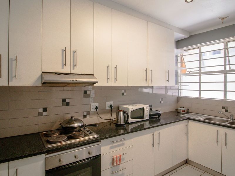 A functional kitchen featuring white cabinetry, granite countertops, a built-in oven with hob, and a tiled backsplash with a window providing natural light.