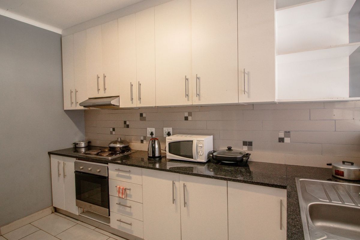 A functional kitchen featuring white built-in cabinetry, dark granite countertops, a tiled backsplash, and integrated stainless steel oven and hob.