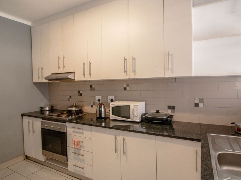 A functional kitchen featuring white built-in cabinetry, dark granite countertops, a tiled backsplash, and integrated stainless steel oven and hob.