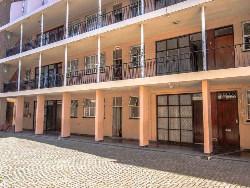 Exterior view of a multi-story apartment block featuring a paved courtyard, shared balconies with wrought iron railings, and multiple unit entrances.