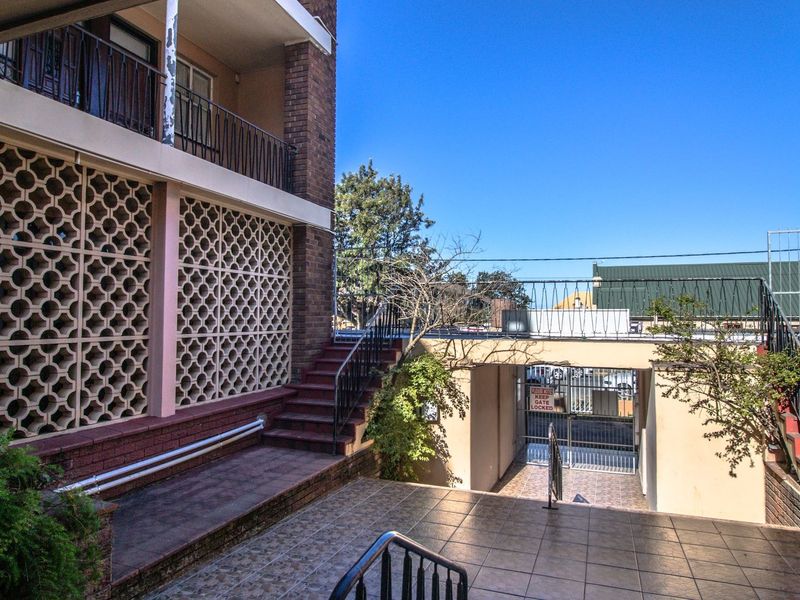 Exterior view of a multi-level apartment complex featuring brick facade, decorative breeze block screens, tiled staircases, and secure gated access.