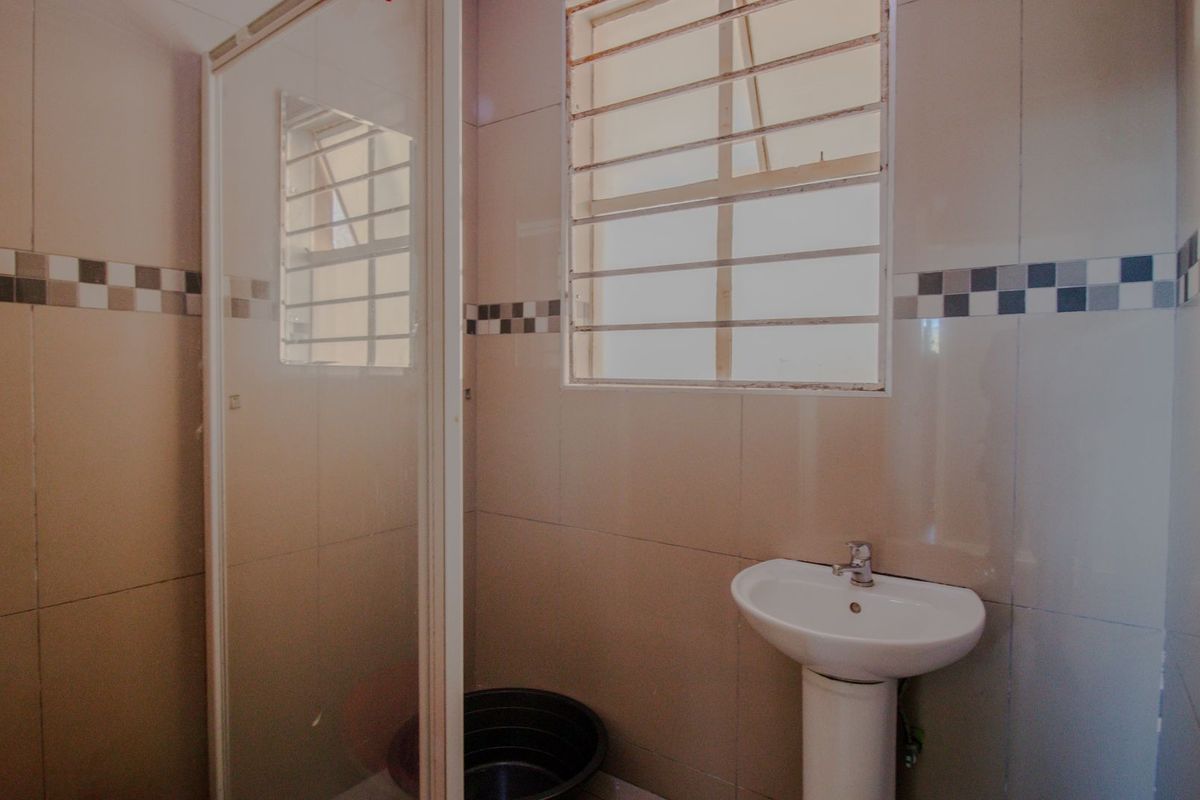 A functional bathroom featuring a pedestal basin, shower enclosure, and tiled walls with security bars on the window.