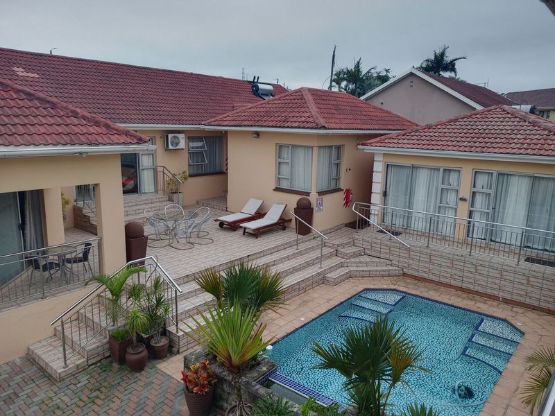 Rear exterior view featuring a multi-level tiled patio, swimming pool, and access to multiple living areas via sliding glass doors.
