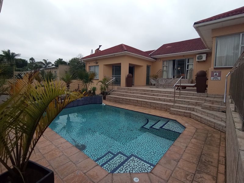A well-maintained outdoor pool area featuring a tiled swimming pool, raised patio with steps, and access to the main house structure.