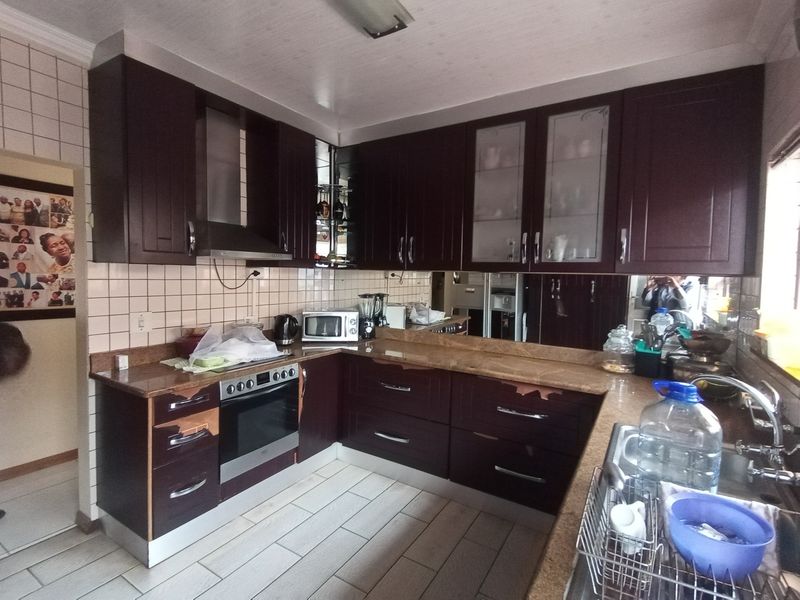 A functional kitchen featuring dark wood cabinetry, granite countertops, and a tiled backsplash, showing signs of wear on the cabinet finishes.