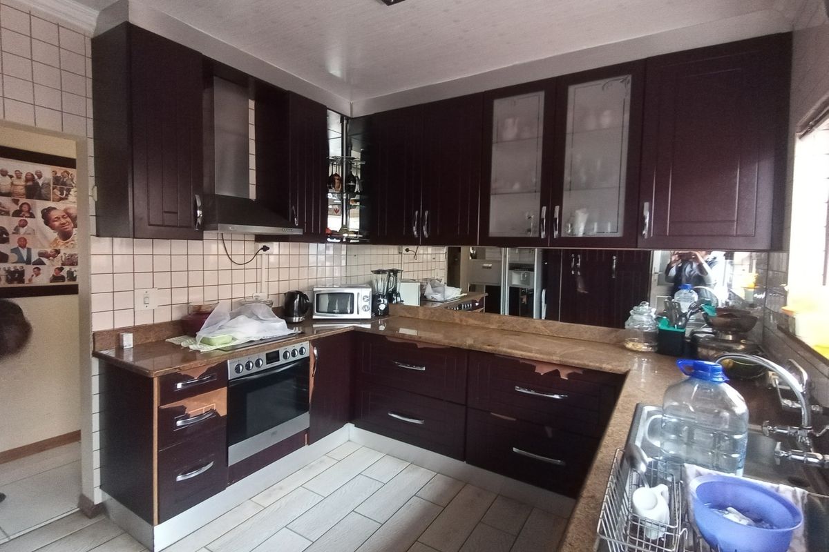 A functional kitchen featuring dark wood cabinetry, granite countertops, and a tiled backsplash, showing signs of wear on the cabinet finishes.