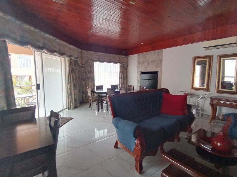 Open-plan living and dining area featuring a distinctive wood-paneled ceiling, tiled floors, a built-in fireplace, and direct access to an outdoor patio.