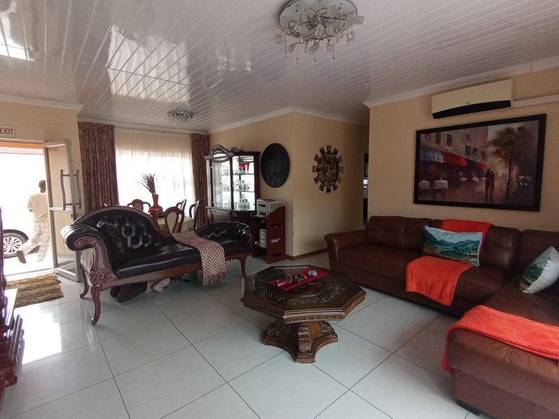 Spacious living room featuring large format floor tiles, a glossy panelled ceiling, and a wall-mounted air conditioning unit.